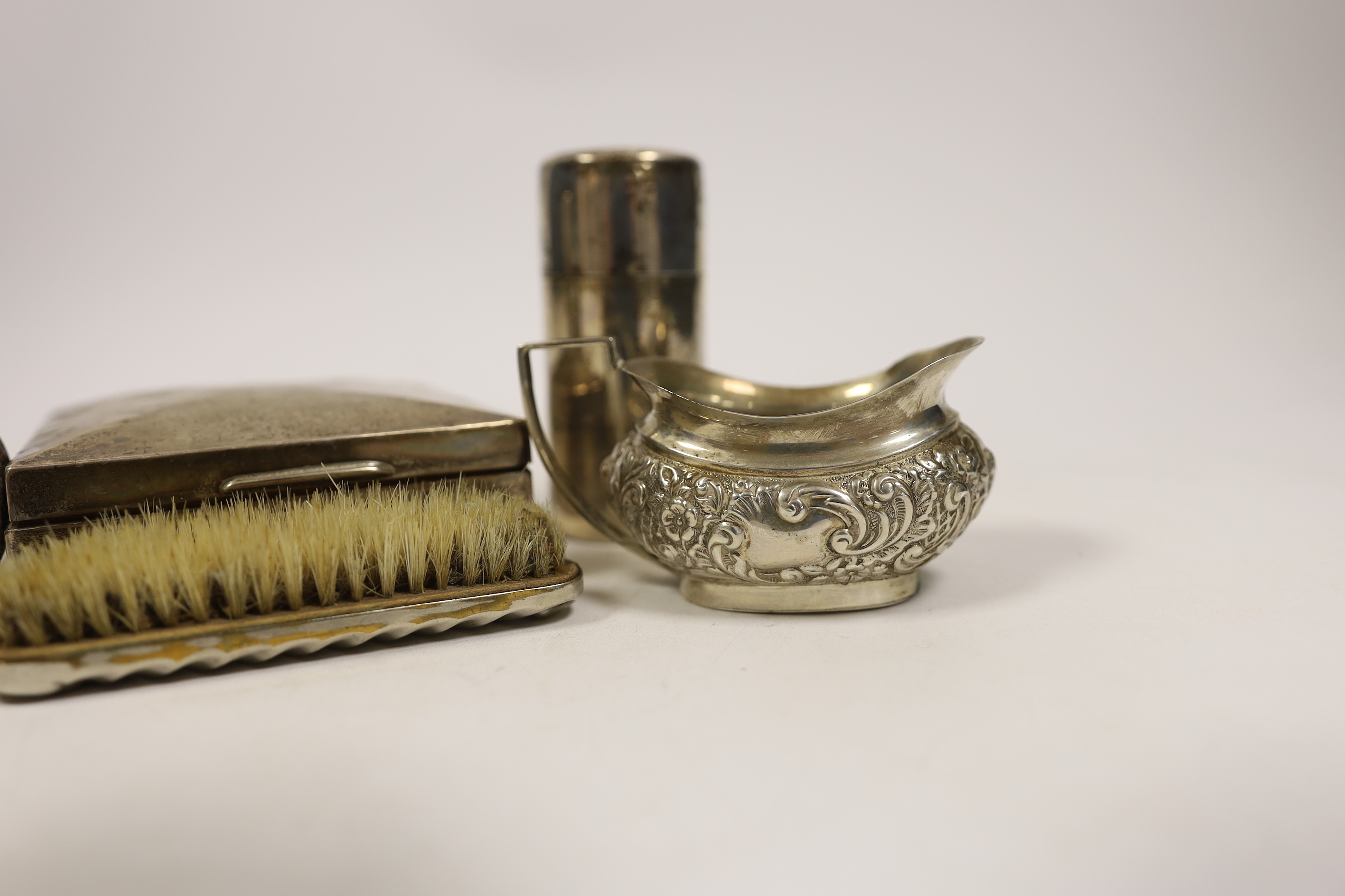 A late Victorian embossed silver cream jug, a pair of silver toilet bottles, a silver backed brush, a silver cigarette box and two other items.